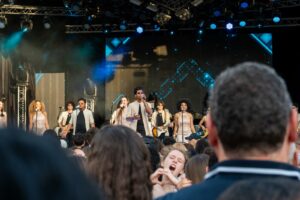 Photographie de concert live à Asnières, groupe de chanteurs et musiciens sur scène avec public au premier plan, reportage événementiel musical.