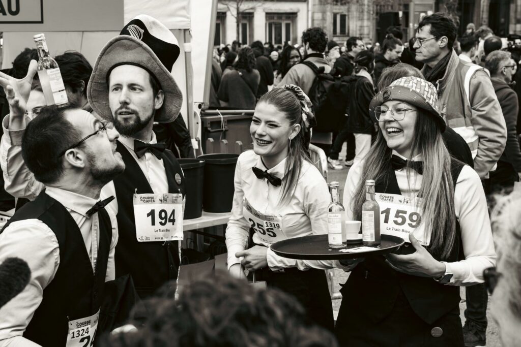 Suggestion : Photographie de groupe en noir et blanc de serveurs et serveuses souriants avant la Course des Cafés à Paris, portraits lifestyle événementiels.