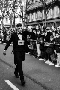 Portrait en noir et blanc d'un serveur élégant en costume lors de la Course des Cafés à Paris, reportage photo de rue et traditions parisiennes.