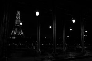 Vue de nuit en noir et blanc de la Tour Eiffel illuminée, encadrée par les colonnes métalliques du pont de Bir-Hakeim à Paris.