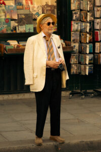 Portrait de rue d'un homme élégant en costume vintage et chapeau devant un kiosque à journaux à Paris.