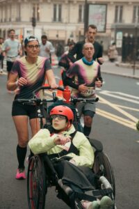 Photographie de reportage sportif, inclusion au Semi-marathon de Paris : femme poussant un jeune en fauteuil roulant tout-terrain, moment de solidarité urbaine.