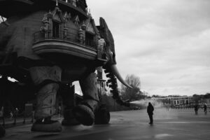 Photographie en noir et blanc du Grand Éléphant des Machines de l'Île à Nantes projetant de l'eau sur un passant.