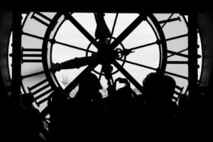Silhouette de l'horloge du Musée d'Orsay en noir et blanc avec vue sur la basilique du Sacré-Cœur et des visiteurs en contre-jour.