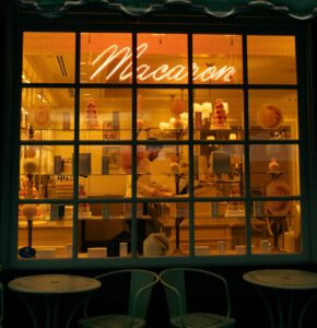 Vitrine illuminée d'une pâtisserie affichant une enseigne au néon Macaron et des pyramides de macarons colorés à l'intérieur.