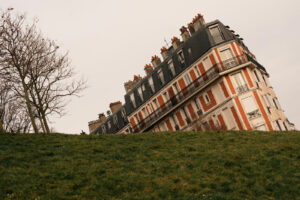 Illusion d'optique d'un immeuble parisien en briques rouges semblant s'enfoncer dans une colline herbeuse à Montmartre.