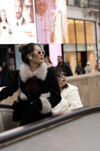 Portrait de rue d'une femme élégante avec des lunettes de soleil vintage et un manteau à col de fourrure sur un escalator à Paris.