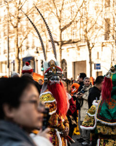 Personnage costumé avec un masque d'opéra de Pékin, une barbe rouge et de longues plumes au défilé du Nouvel An Lunaire à Paris.