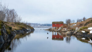 Petite maison de pêcheur rouge sur pilotis au bord d'un fjord en Norvège avec reflet dans l'eau