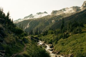 Un sentier de randonnée escarpé longeant un torrent de montagne avec des sommets rocheux et des névés en arrière-plan dans les Rocheuses canadiennes.