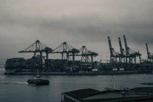 Un ferry SeaBus naviguant dans le port de Vancouver devant des grues de chargement de conteneurs sous un ciel gris et industriel.