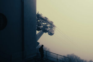 Silhouette d'un homme de dos contemplant les cabines du téléphérique de Grenoble disparaissant dans un brouillard épais.